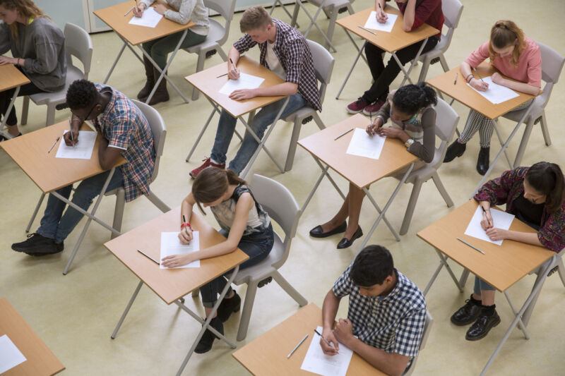 Overhead view of a classroom full of students at desks, focused on writing on papers.